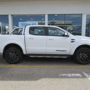 Side view of a white Ford Ranger 3.2 pickup truck with black alloy wheels parked outside a dealership.